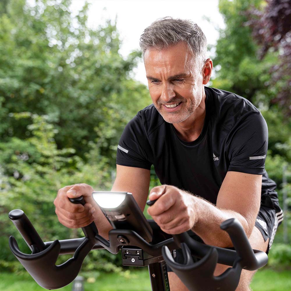 Man smiling while riding IC7 exercise bike in backyard