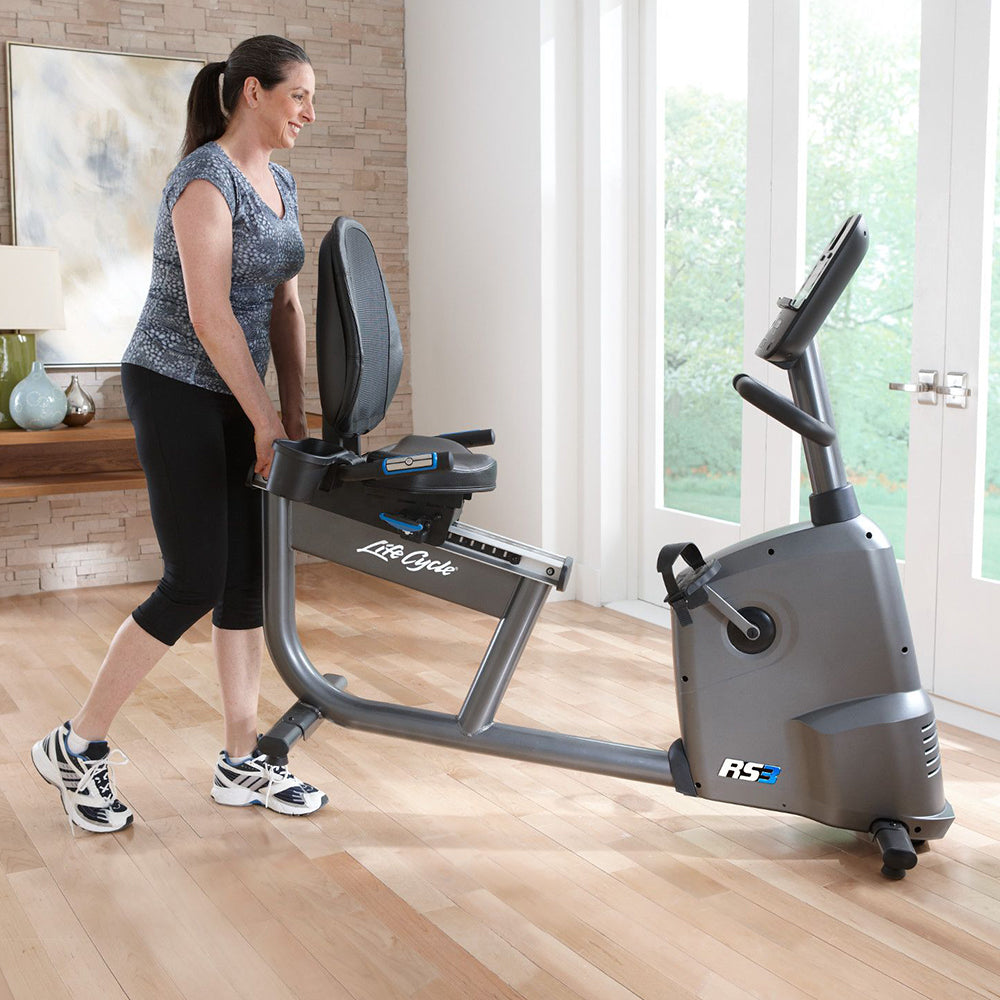 Female lifting back of Life Fitness RS3 Recumbent LifeCycle bike on front wheels